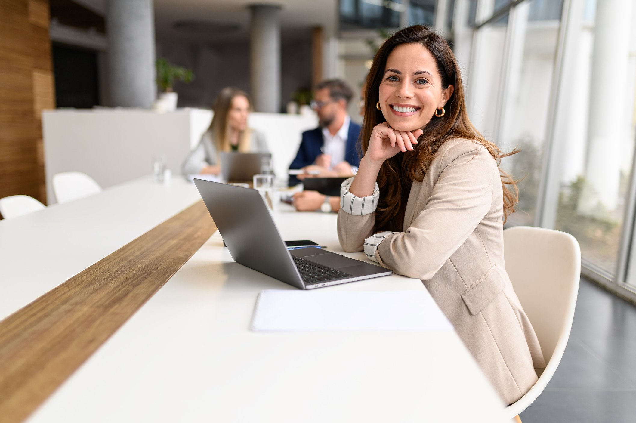 Person sat at a desk with an open laptop. They are turned towards the camera smiling. Person sat at a desk with an open laptop. They are turned towards the camera smiling.